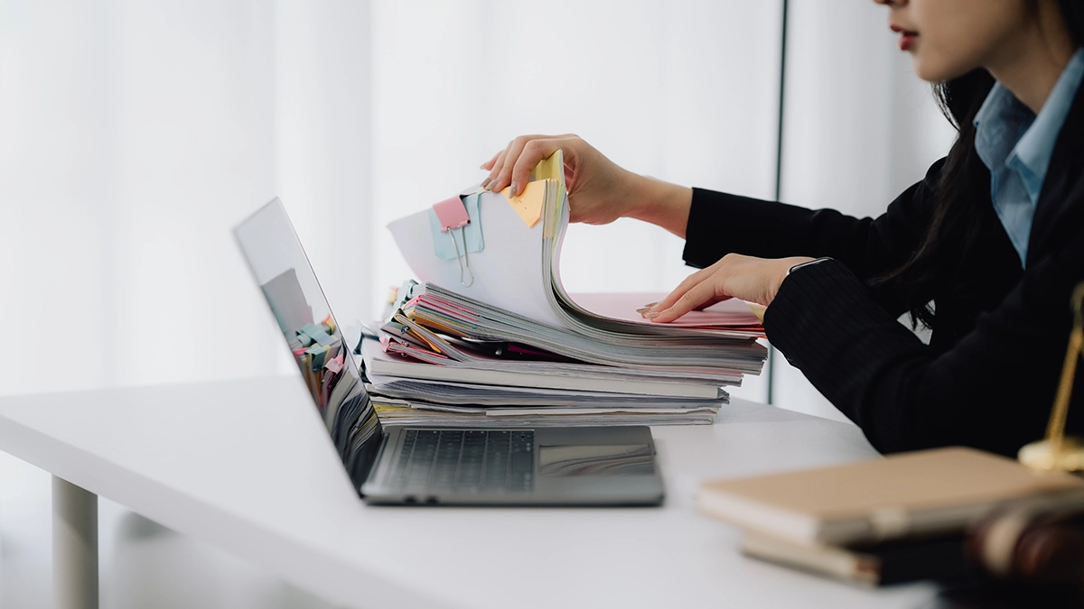 Compliance-medarbejder gennemgår en stak af tekniske dokumenter ved arbejdsstation