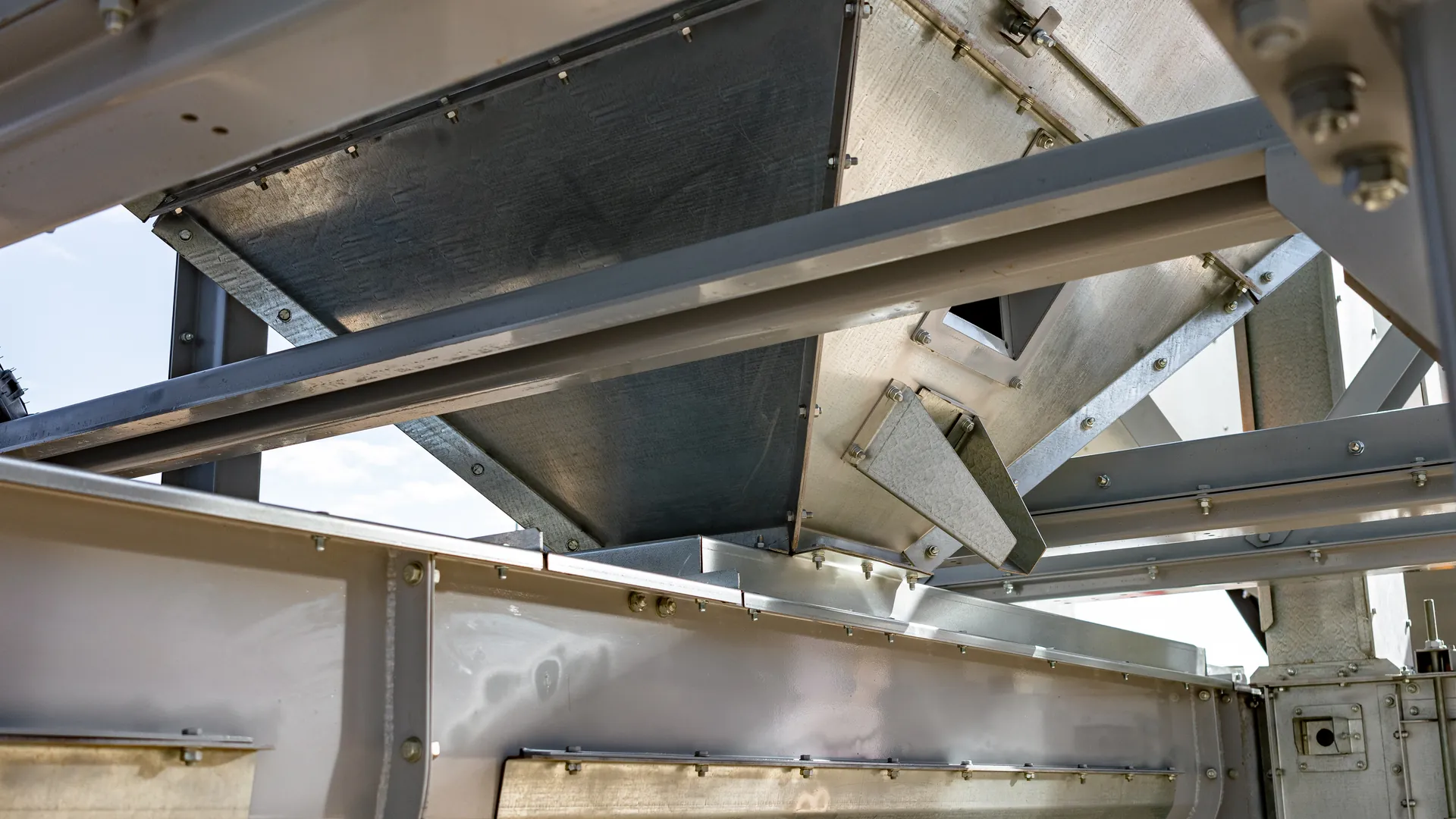 Undersiden af en industriel tragt, der t&oslash;mmer ud i en bred metalrende, b&aring;ret af galvaniserede st&aring;ldragere
